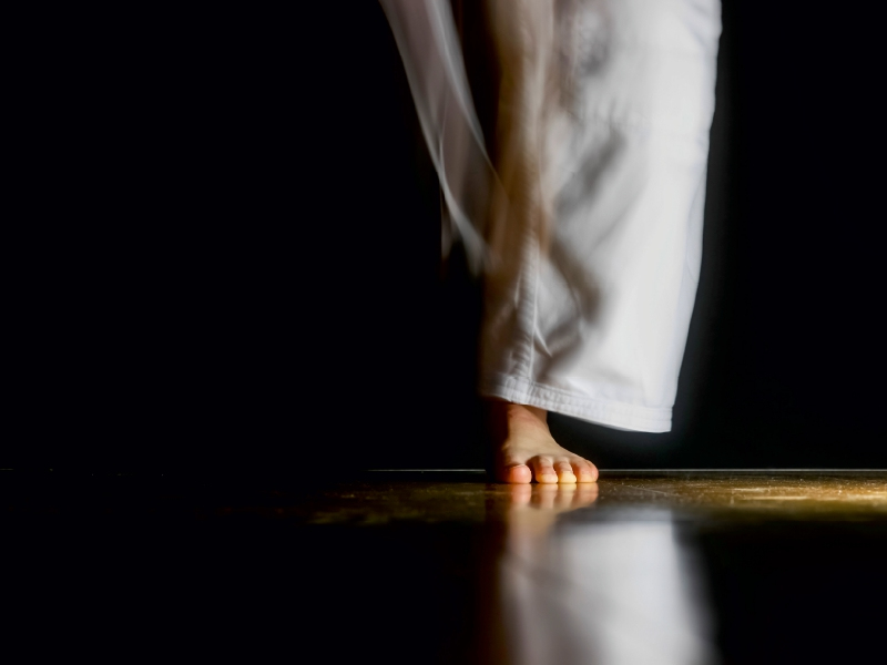 Unschärfe einer Person in weißer Hose, die auf einem Holzfußboden steht, vor schwarzem Hintergrund.