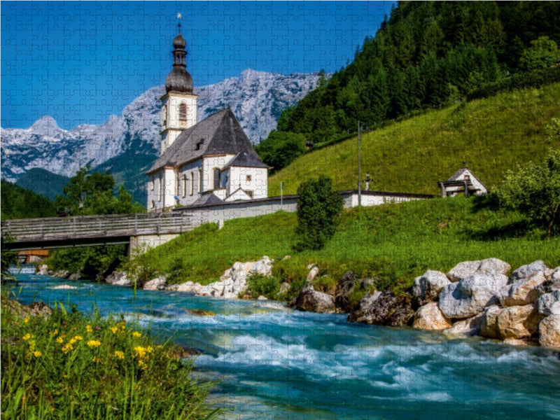 Ein reißender blauer Fluss fließt an einem grünen Hang mit einer traditionellen Kirche und Bergen vorbei.