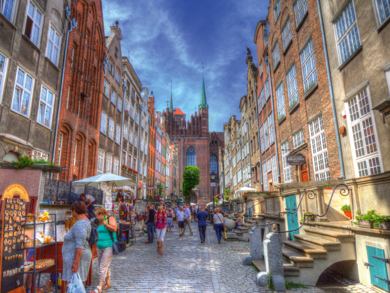 Belebte historische Kopfsteinpflasterstraße mit Geschäften und Fußgängern, eingerahmt von alten Backsteingebäuden.
