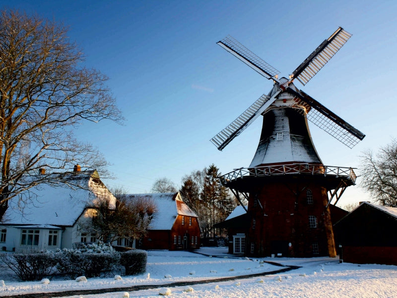 Eine Windmühle und verschneite Häuser an einem sonnigen Wintertag mit blauem Himmel.