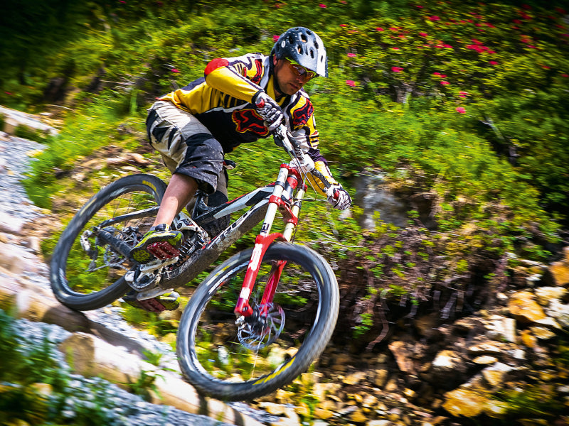 Ein Mountainbiker fährt auf einem steilen, felsigen Waldweg bergab.