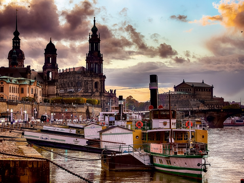 Dampfschiff am Elbufer in Dresden bei Sonnenuntergang mit historischen Gebäuden im Hintergrund.