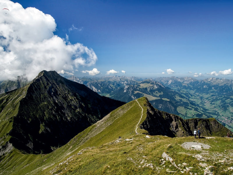 Panoramablick auf grüne Berggipfel unter blauem Himmel mit weißen Wolken und einem Wanderweg.