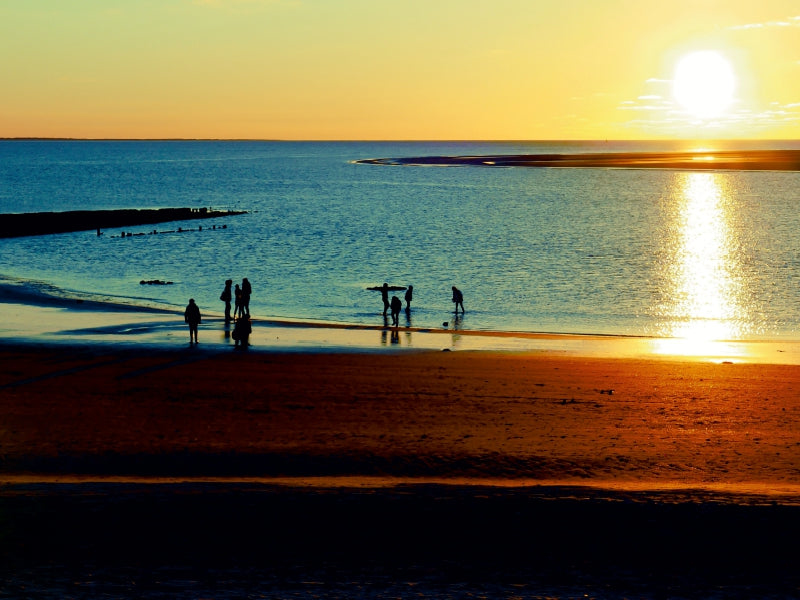 Silhouetten von Menschen am Strand bei Sonnenuntergang mit glitzerndem Meer.