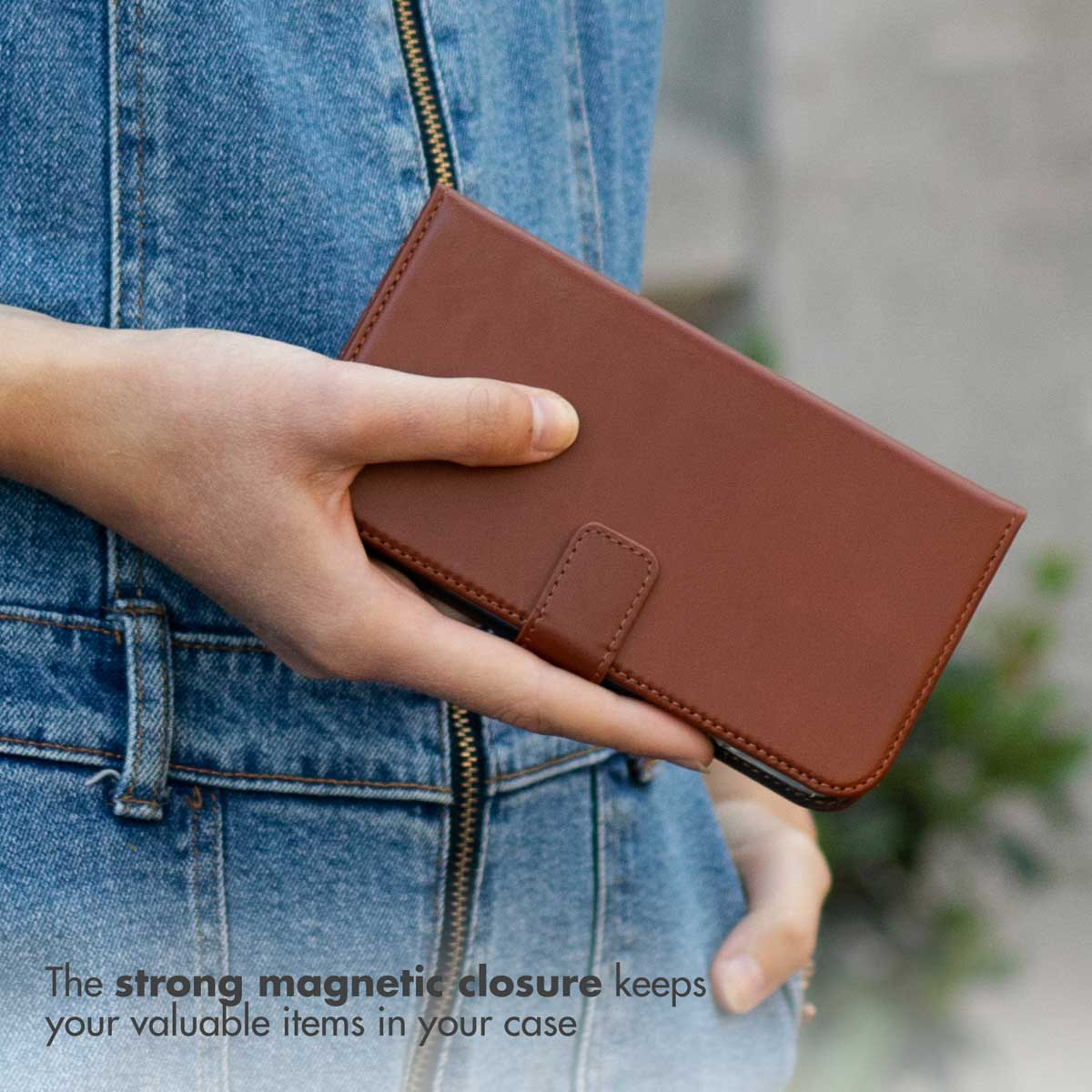 Personne en jean bleu tenant un étui de smartphone en cuir marron fermé.