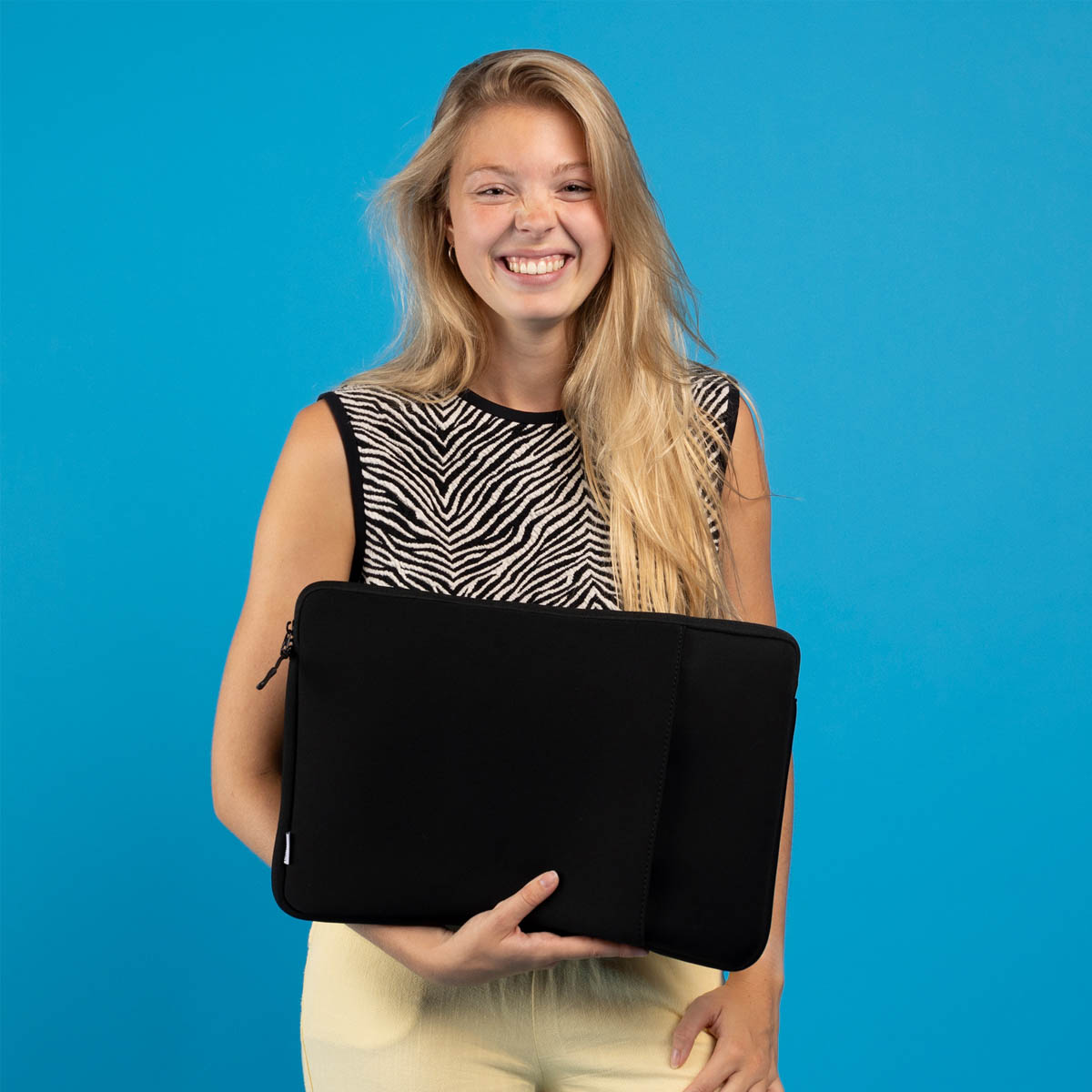 Mujer rubia sonriente sosteniendo una funda negra para portátil sobre fondo azul.