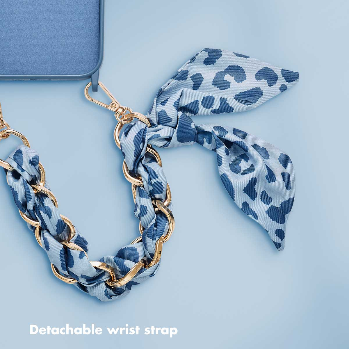 Eine blaue Handyhülle mit abnehmbarer Handschlaufe aus Goldketten und blauem Leo-Muster auf hellem Hintergrund.