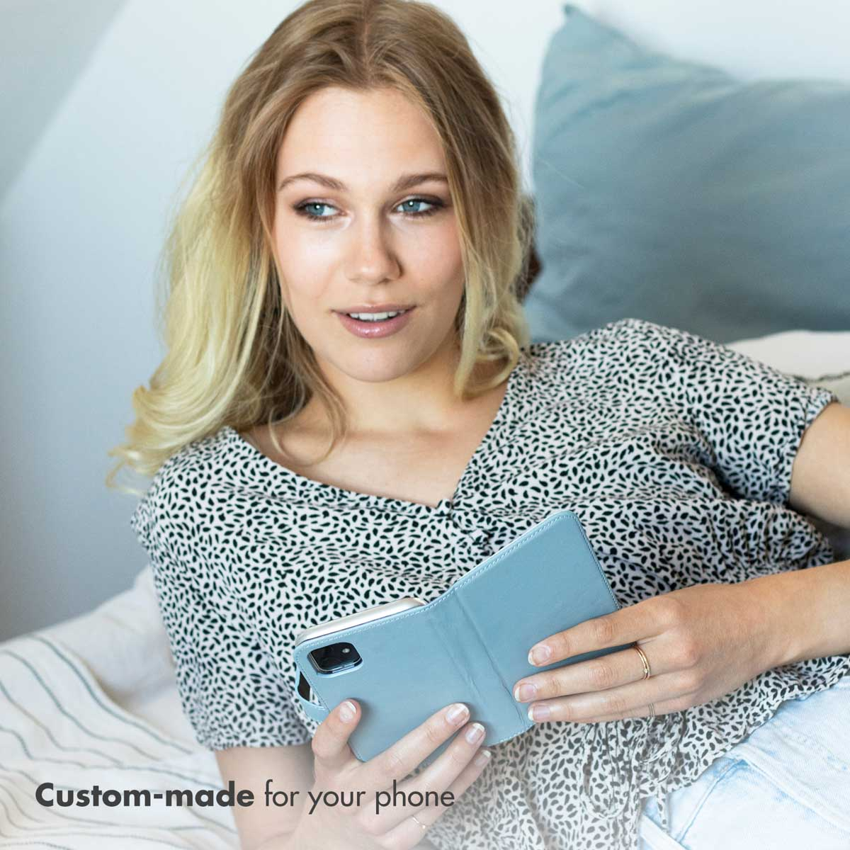Une femme blonde tenant un étui de téléphone bleu dans une chambre.