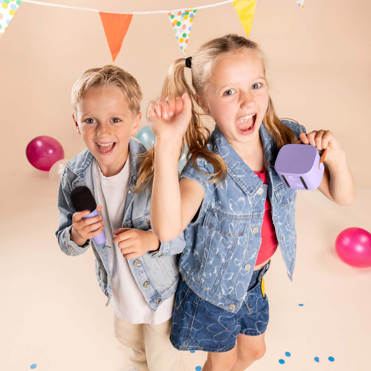 Dos niños felices con chalecos de mezclilla celebran con micrófono y altavoz entre globos.