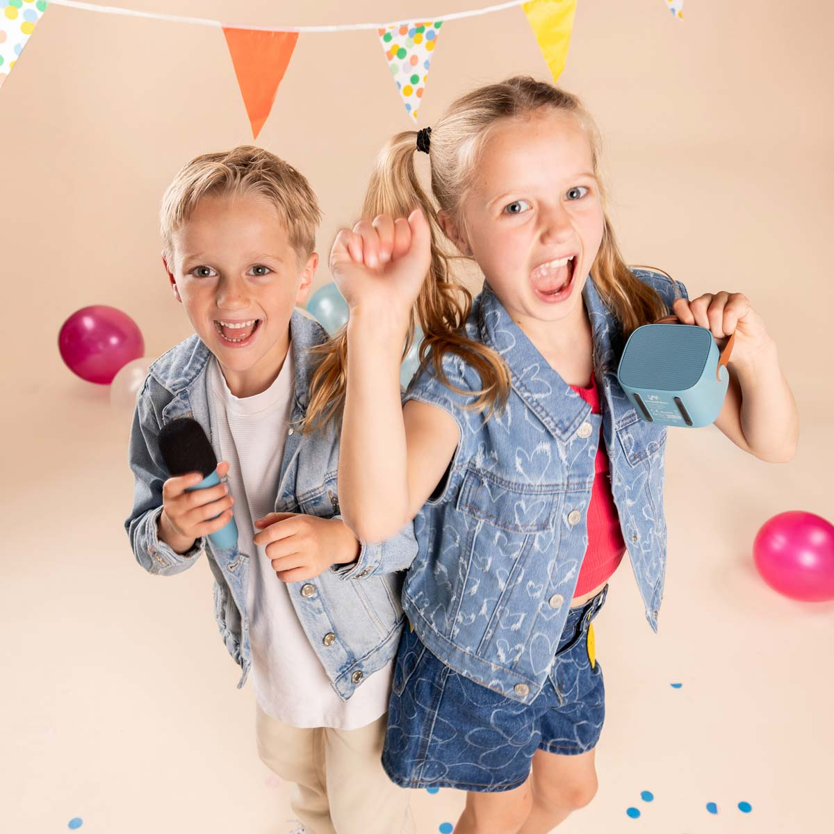 Dos niños felices con ropa de mezclilla celebran con un micrófono y un altavoz entre globos y pancartas.