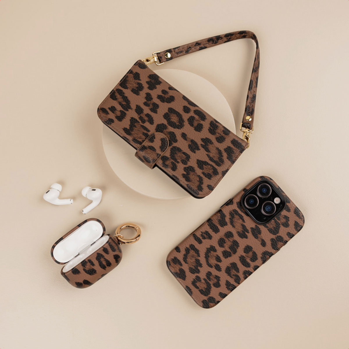 Accessori leopardati: borsa per telefono, cover e custodia per AirPods con auricolari su beige.