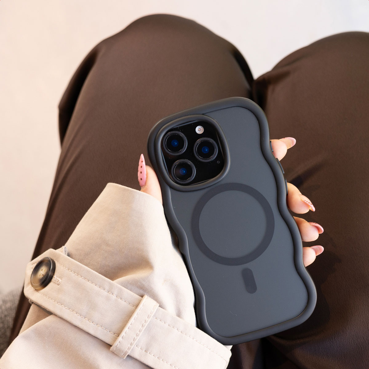 Una mano sostiene un teléfono negro con funda ondulada sobre pantalones oscuros.