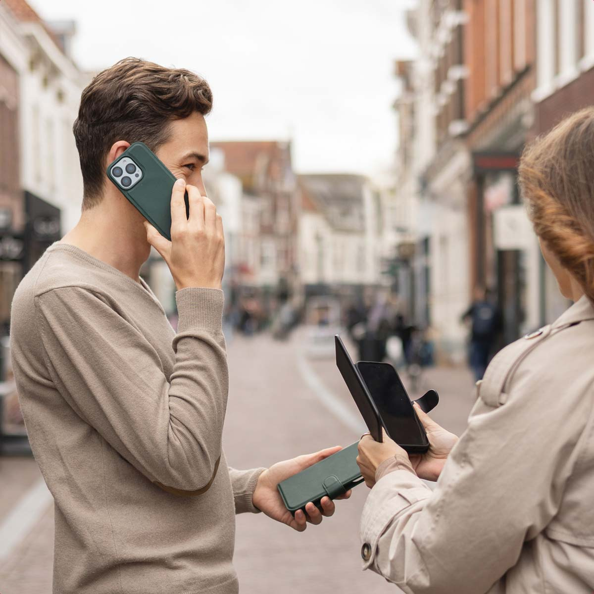 Un uomo parla al suo smartphone in una strada mentre una donna tiene un altro dispositivo.