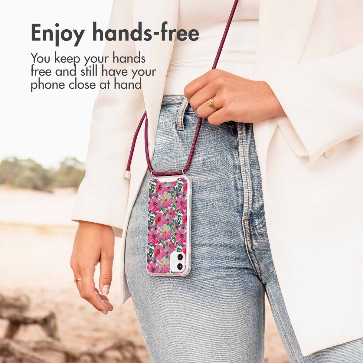 Personne portant un étui de téléphone floral avec une lanière sur un jean bleu et un blazer blanc.