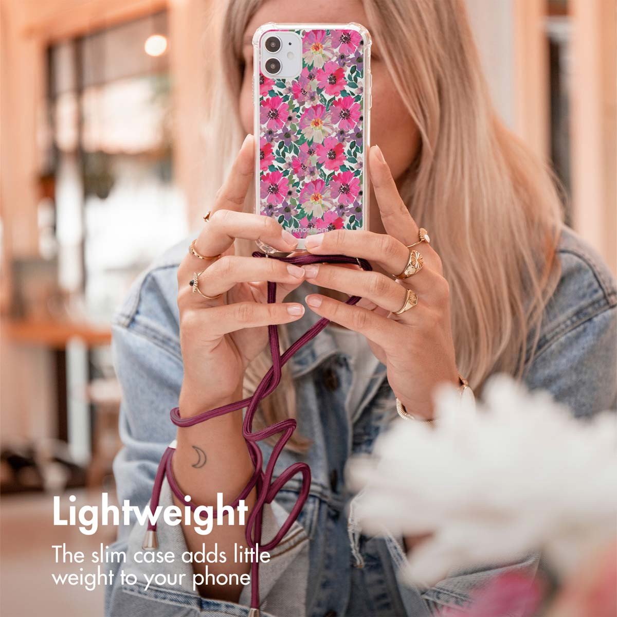 Une femme blonde en veste en jean tient un téléphone avec une coque florale et un lanière violette, avec du texte en bas à gauche.