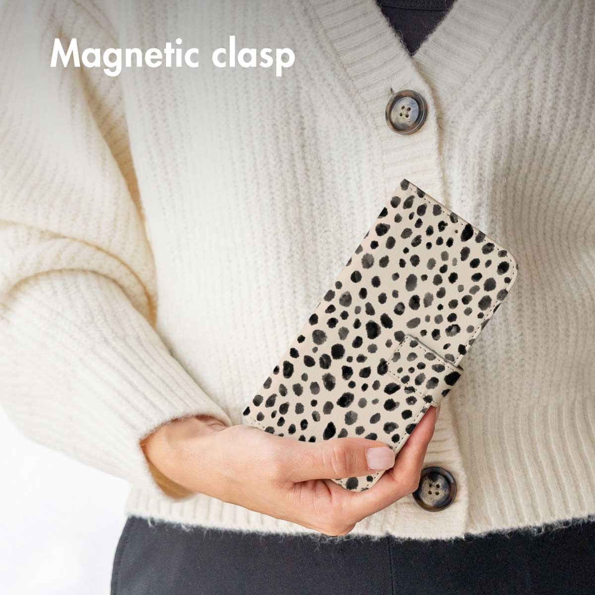 Una persona sostiene una funda de móvil con estampado dálmata y cierre magnético ante un jersey blanco.