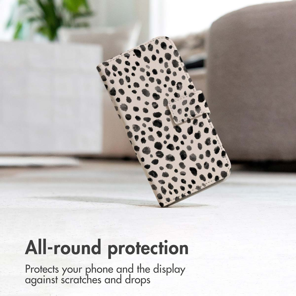 Una funda de móvil beige con manchas negras de dálmata se mantiene erguida sobre una superficie con fondo borroso.