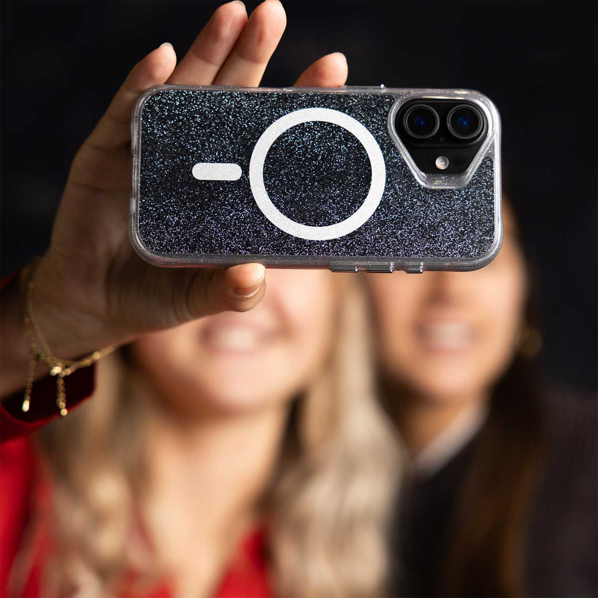 Una mano sostiene un smartphone con funda negra brillante y anillo MagSafe blanco.