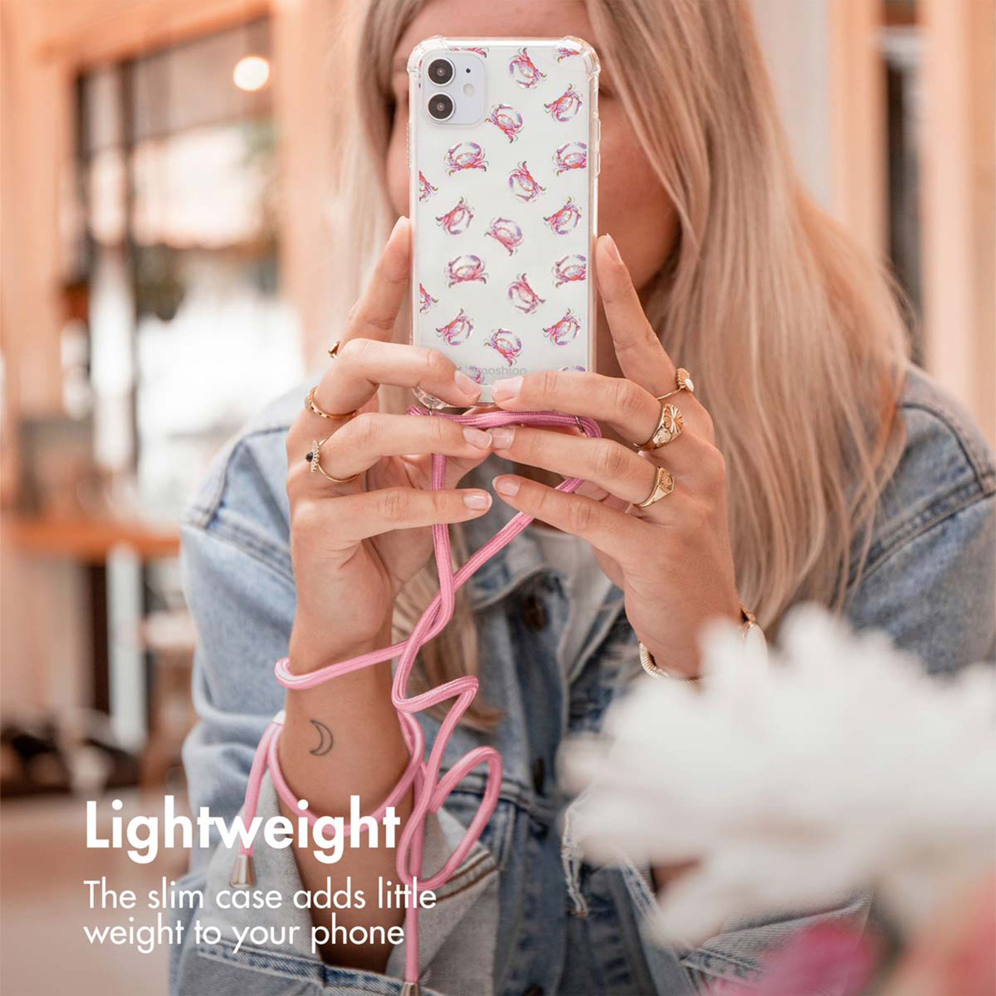 Une femme blonde tient un téléphone dans une coque à motif avec lanière rose.