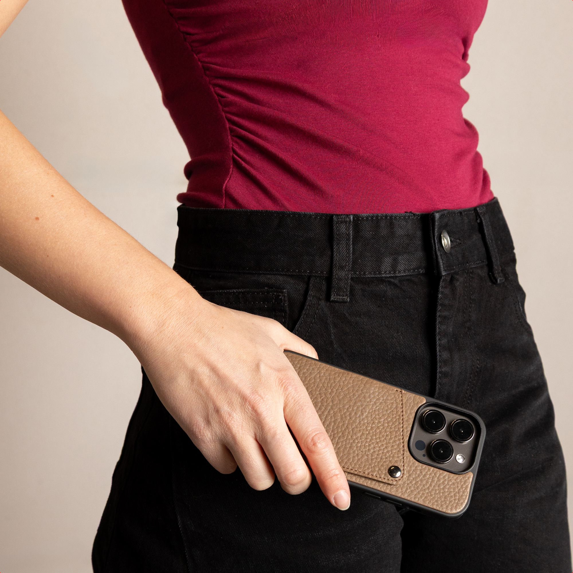 Personne en haut rouge et jean noir tenant un smartphone avec une coque en cuir marron.