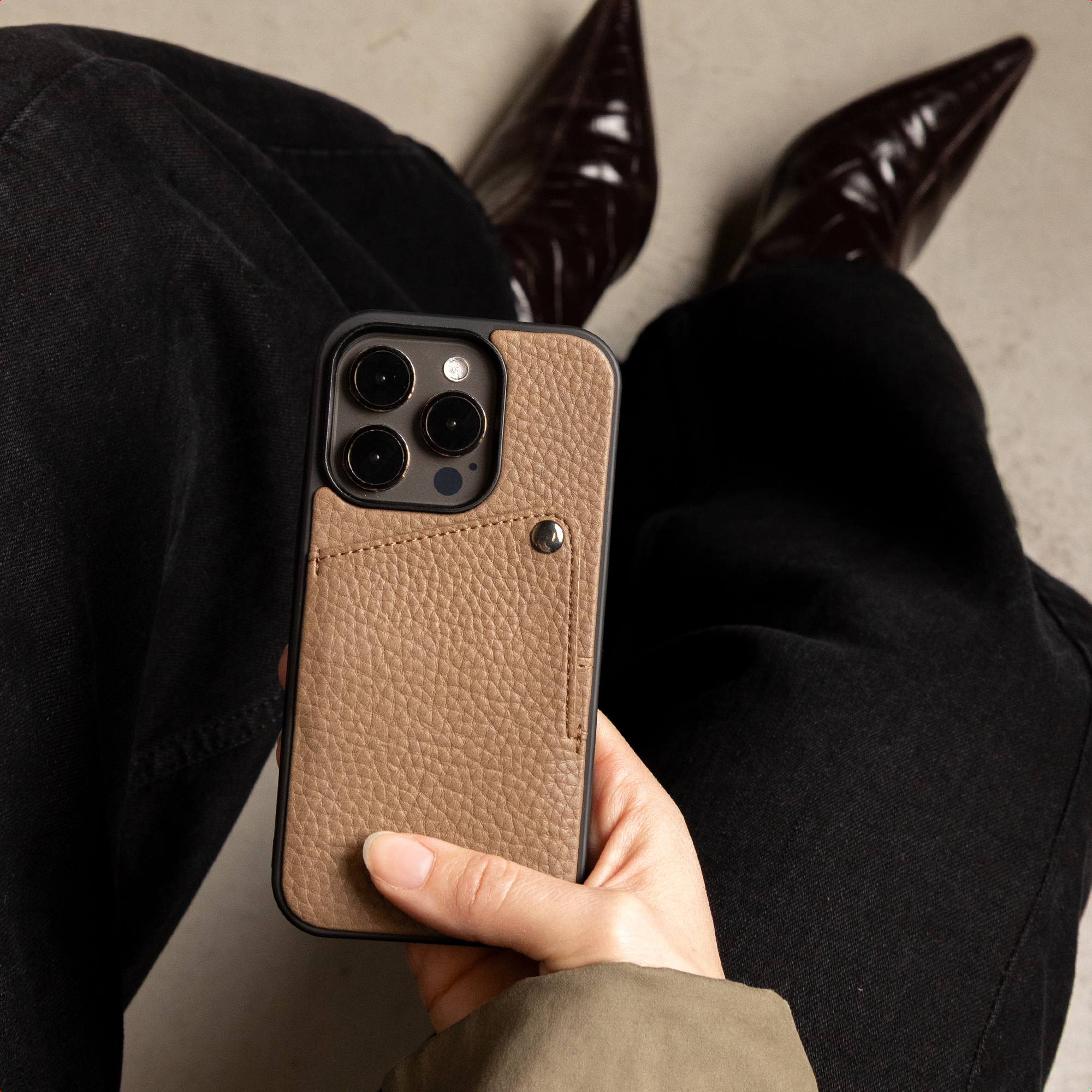 Une main tient un smartphone avec une coque en cuir marron et un porte-cartes.