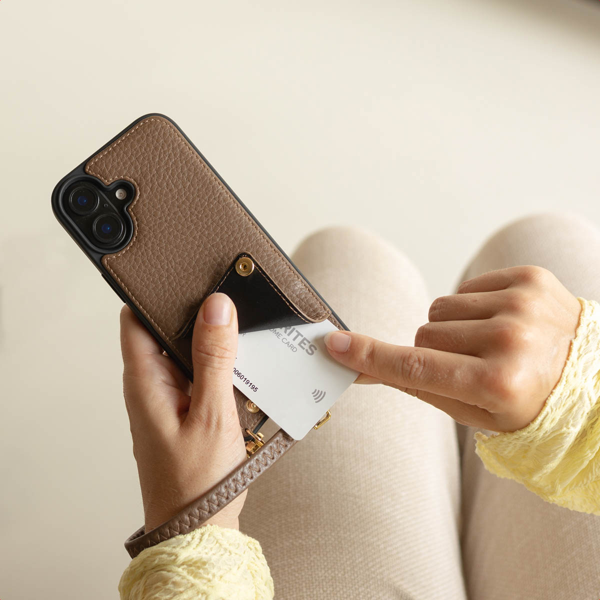 Una persona sostiene un teléfono con funda de cuero marrón y saca una tarjeta del bolsillo trasero.