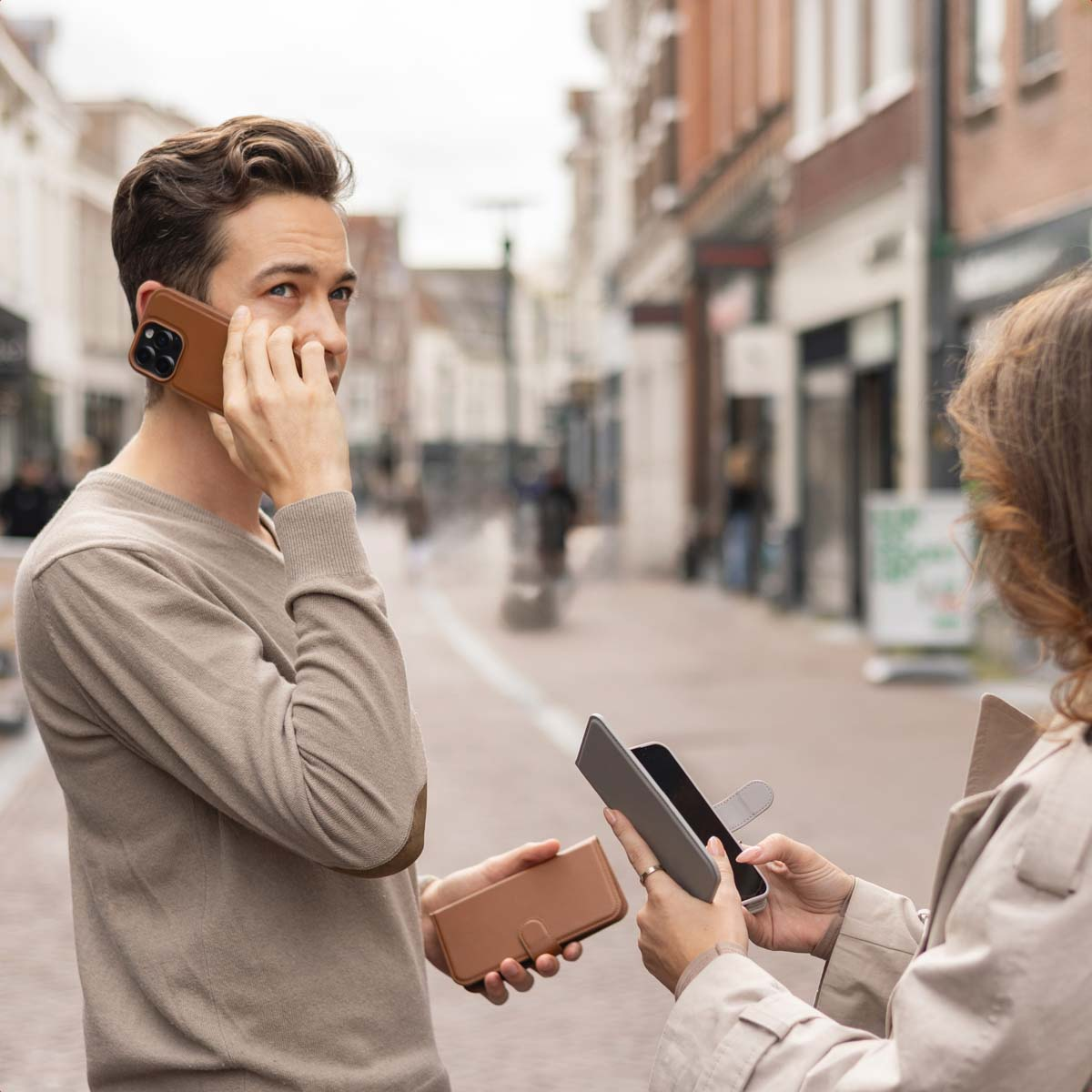 Un uomo parla al telefono in strada mentre una donna tiene uno smartphone con custodia.