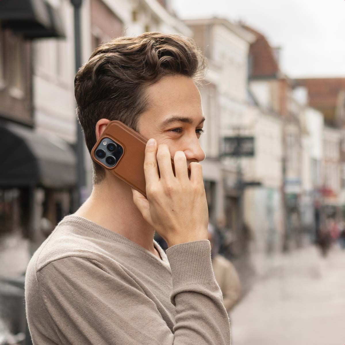 Un uomo con un maglione beige parla al telefono in una strada sfocata.