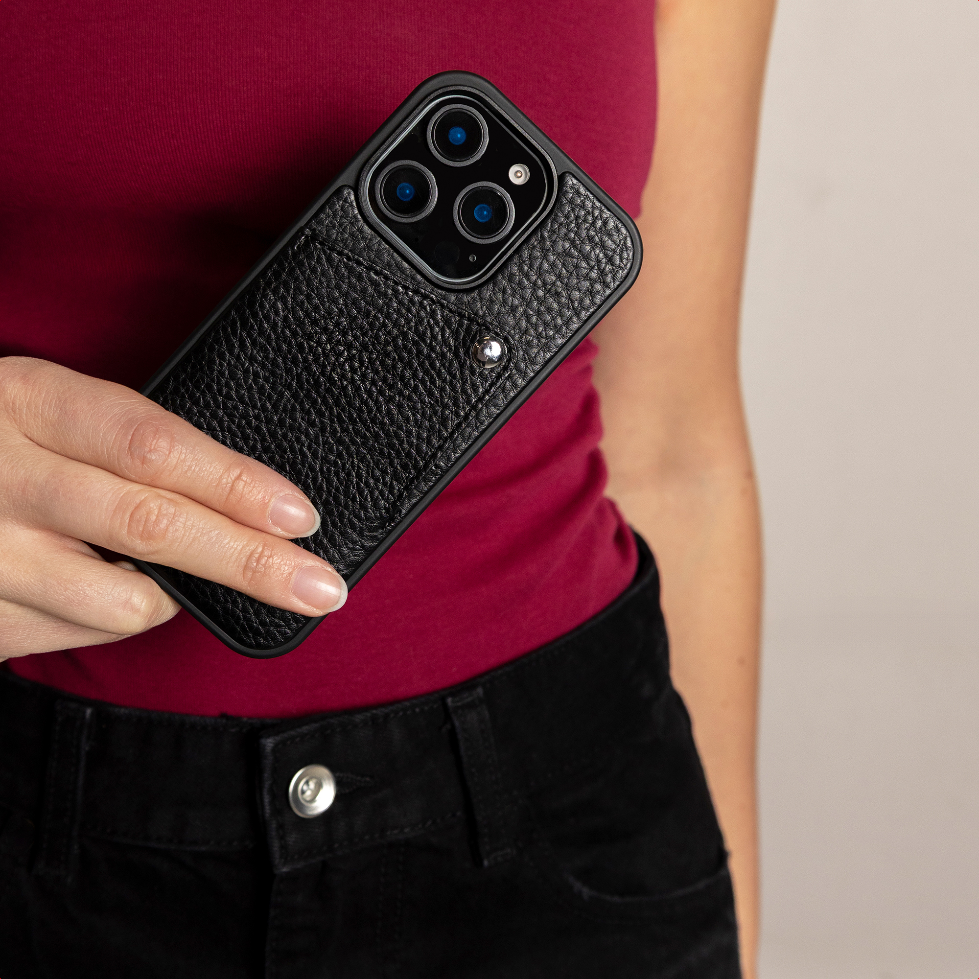 Une femme en haut rouge tient un smartphone en cuir noir avec porte-cartes.