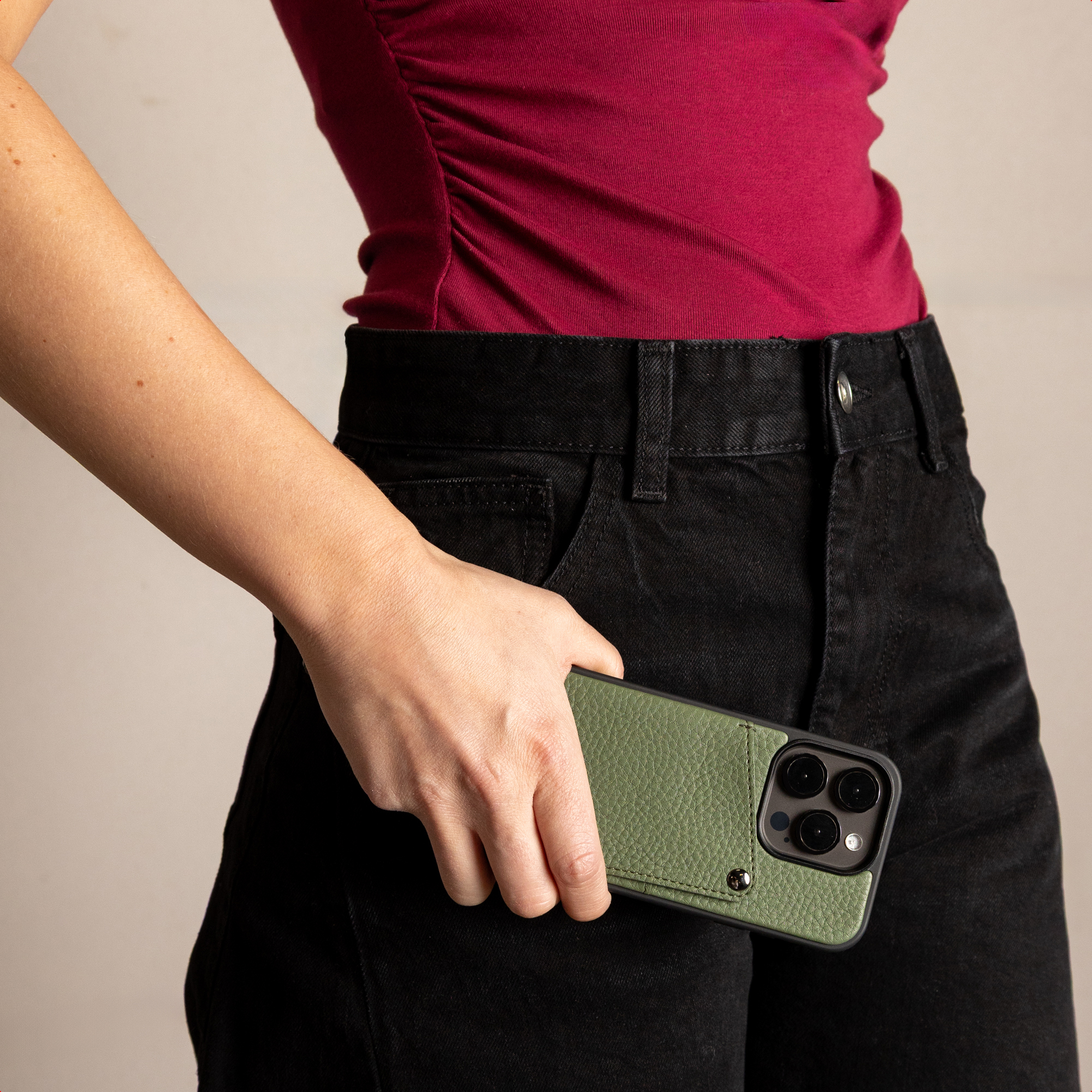 Une personne en chemise rose et pantalon noir tient un smartphone avec coque en cuir vert.