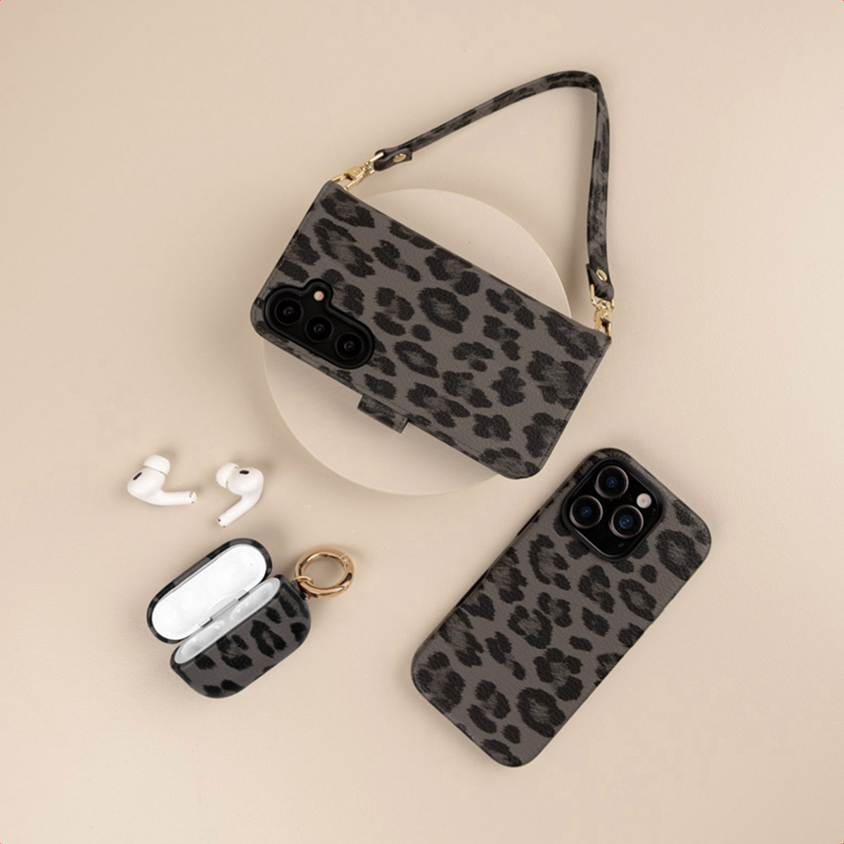 Cover per telefono grigie leopardate con cinturino e custodia per auricolari su beige.