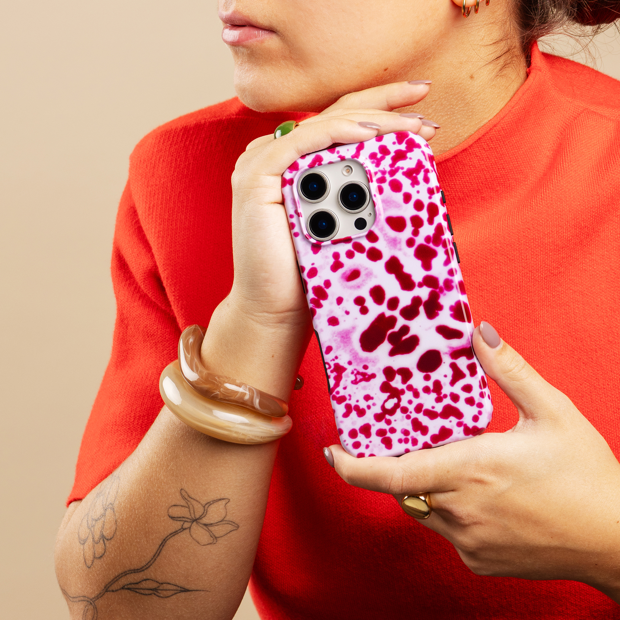 Una mujer con top rojo sostiene un teléfono con manchas rosas y blancas.