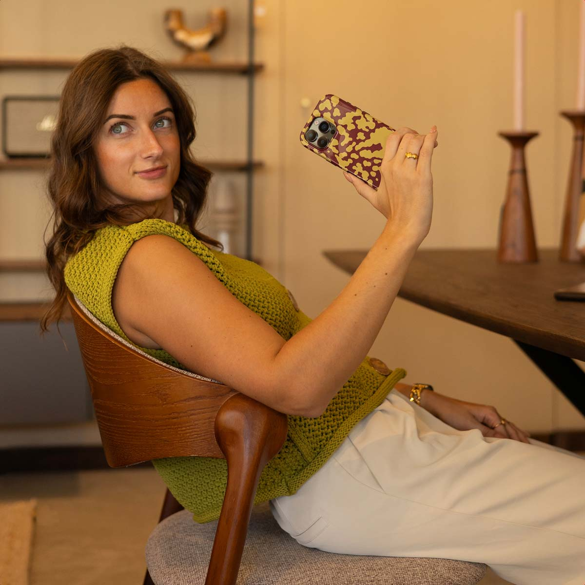 Una donna in top verde tiene uno smartphone con fantasia, scattando una foto.