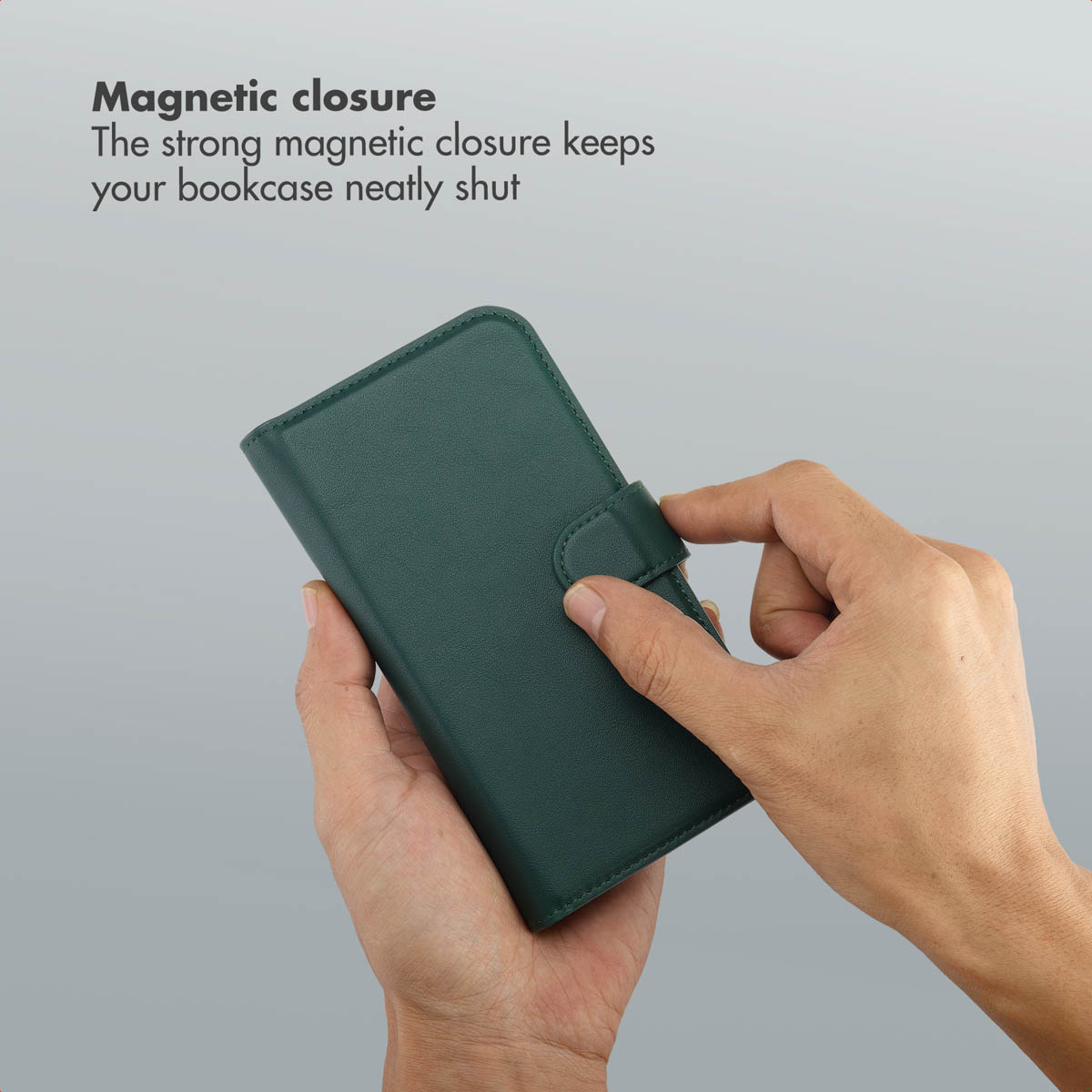 Una mano chiude una custodia in pelle verde per telefono con chiusura magnetica su sfondo grigio.