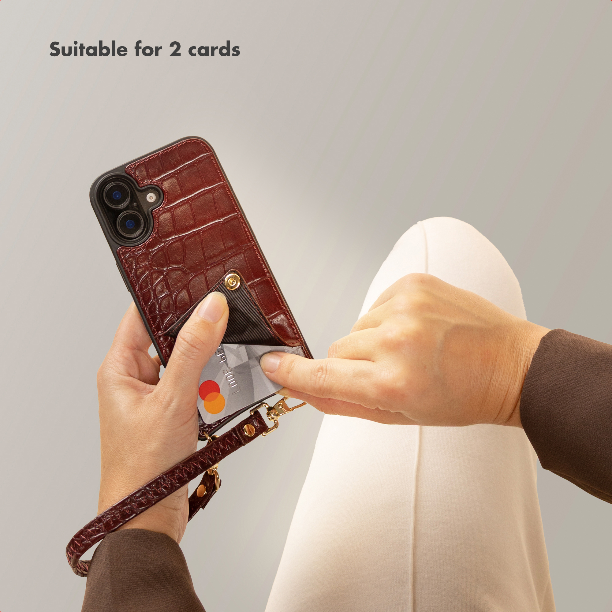 Persona sosteniendo una funda de móvil roja con tarjetero, correa y texto 'Suitable for 2 cards'.