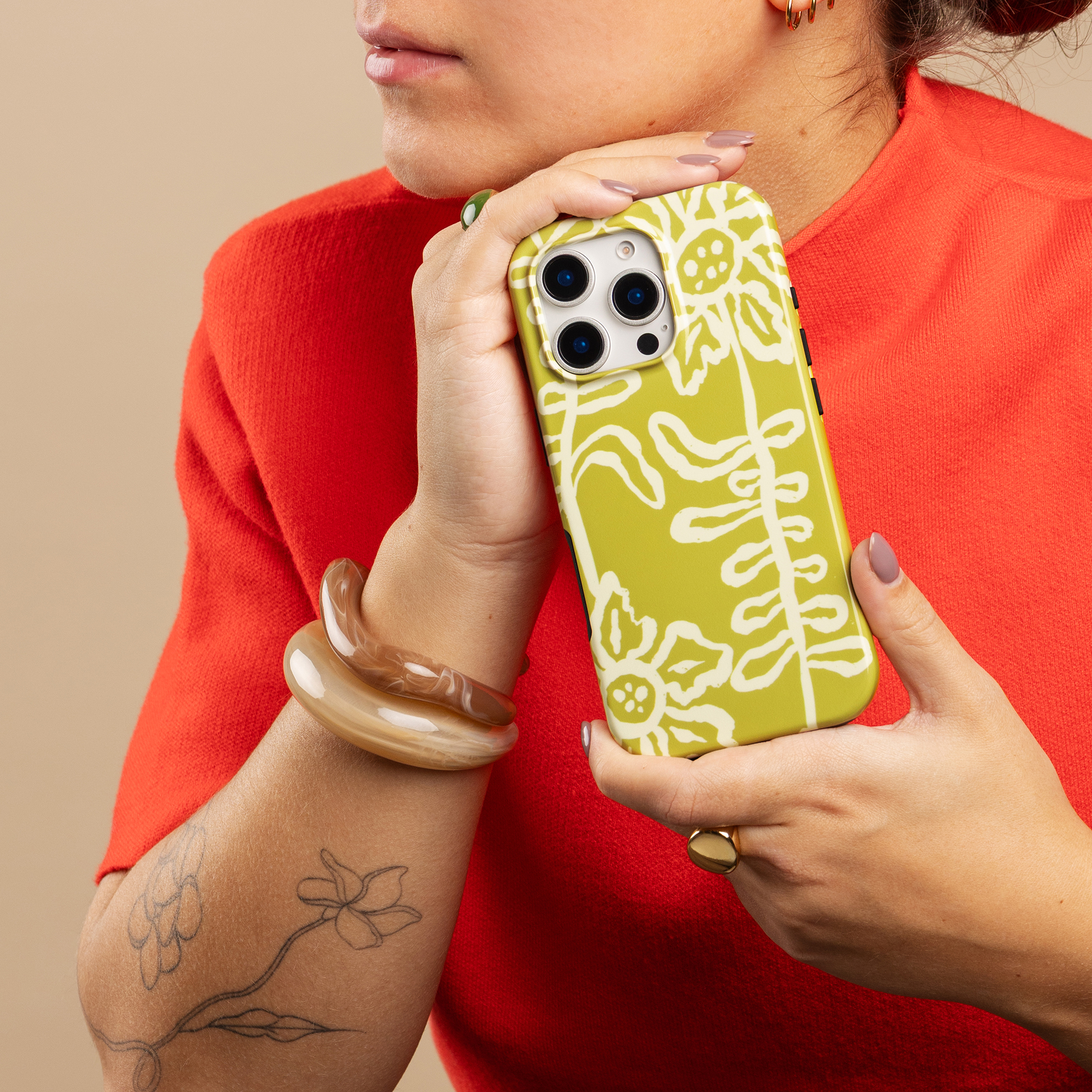 Una mujer con suéter rojo sostiene un smartphone amarillo con estampado floral blanco.