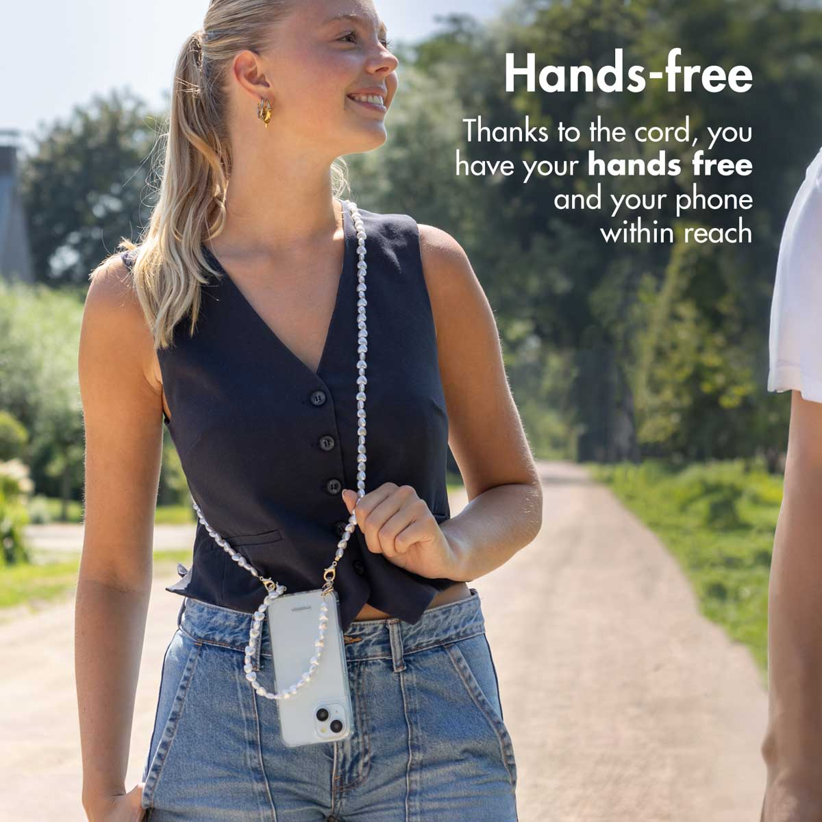Une femme blonde dans un parc porte un téléphone sur un collier de perles autour du cou, avec le texte Hands-free.