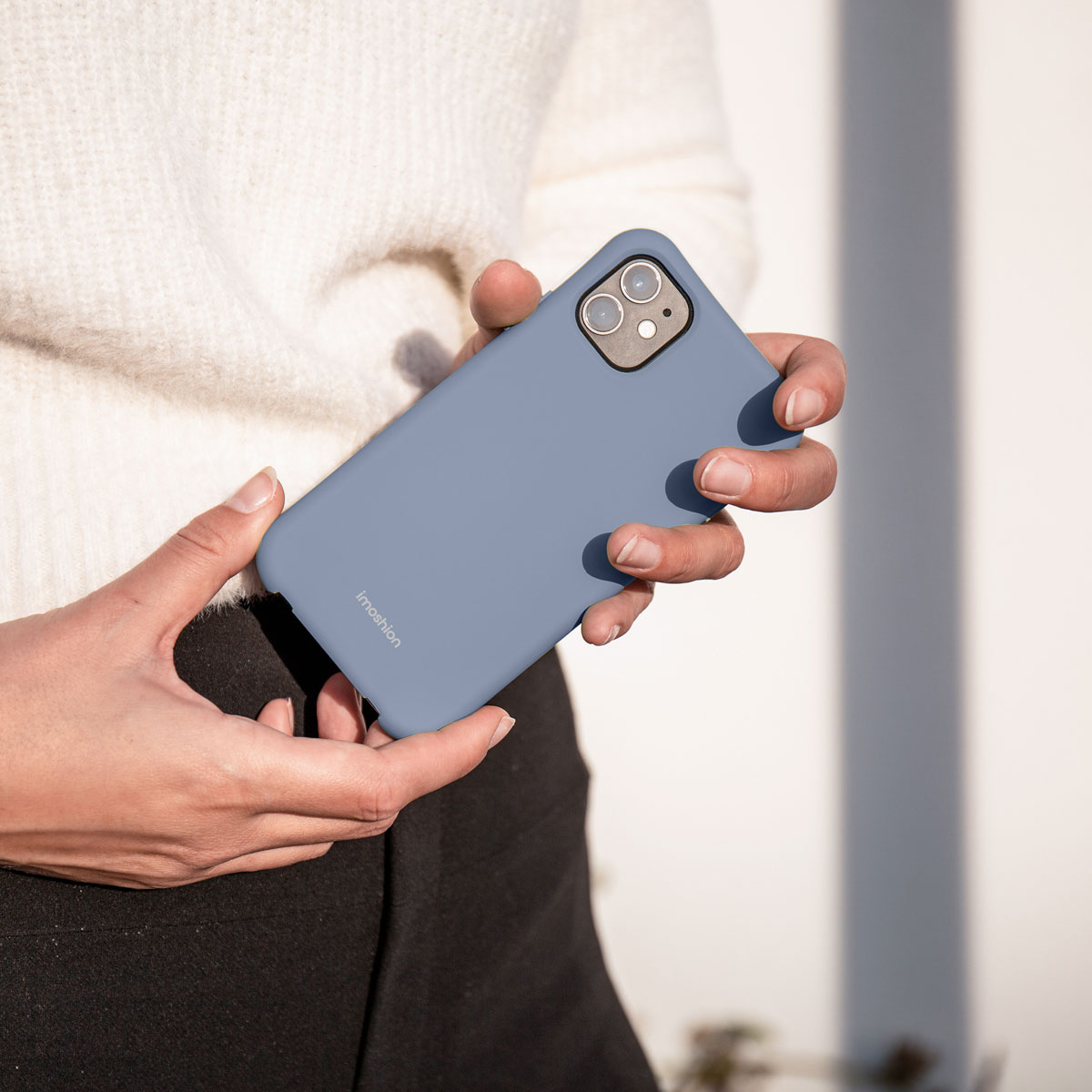 Une personne en pull blanc tient un smartphone bleu dans une coque.