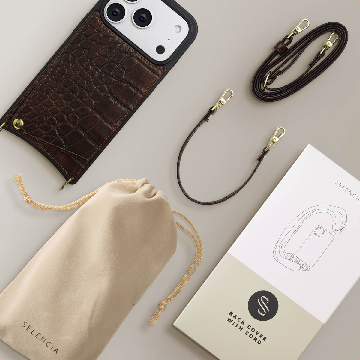 Funda de móvil de cocodrilo, dos correas, bolsa y caja sobre fondo claro.