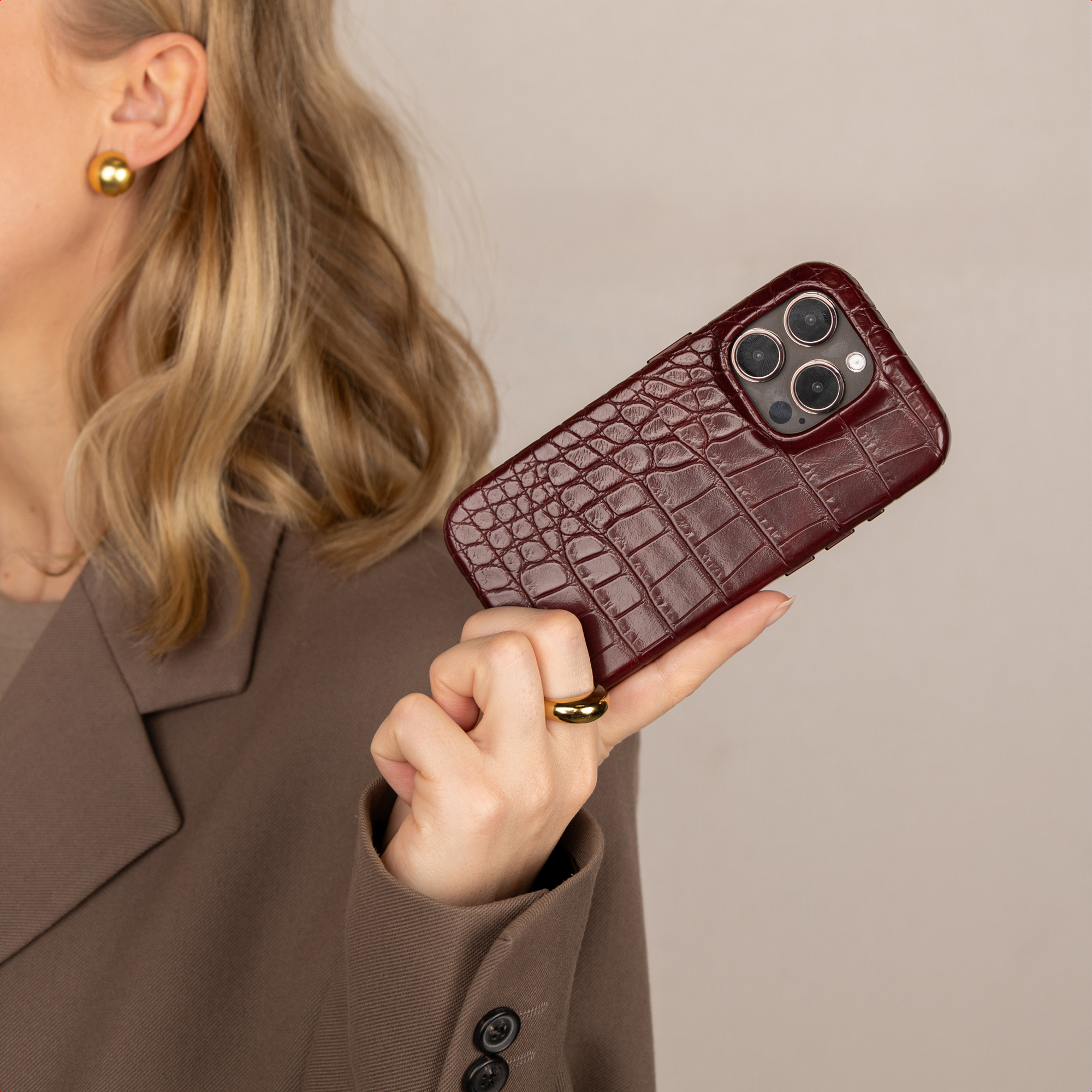 Una donna bionda tiene in mano una custodia per smartphone in pelle di coccodrillo rosso scuro.