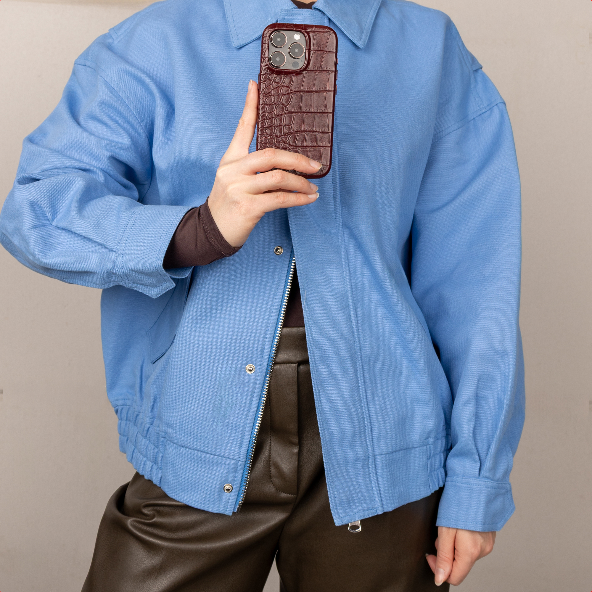 Persona con giacca azzurra e pantaloni di pelle marroni, con in mano un telefono.