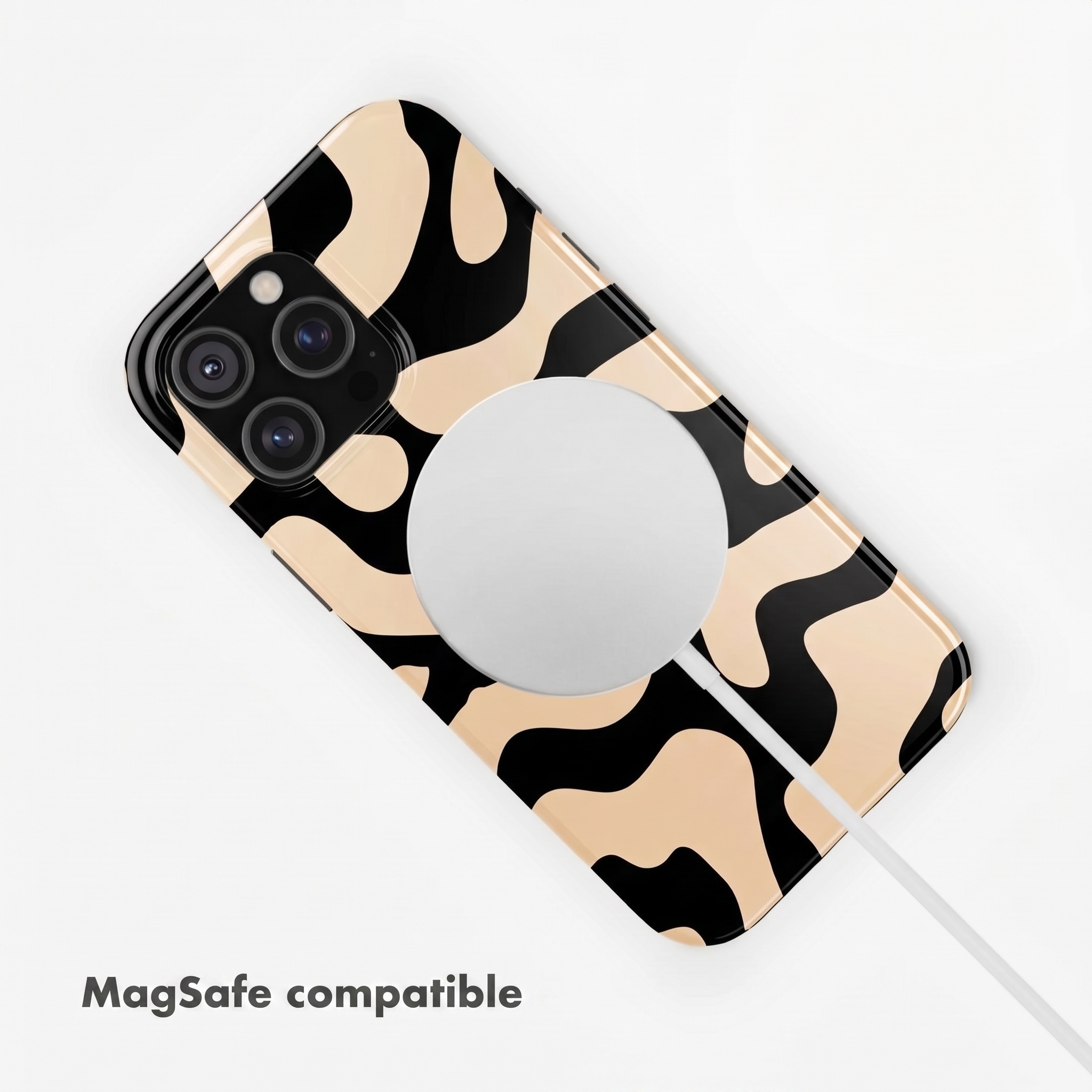 Ein Smartphone in einer schwarz-beigen Fleckenhülle liegt auf weißer Oberfläche mit MagSafe-Ladegerät.