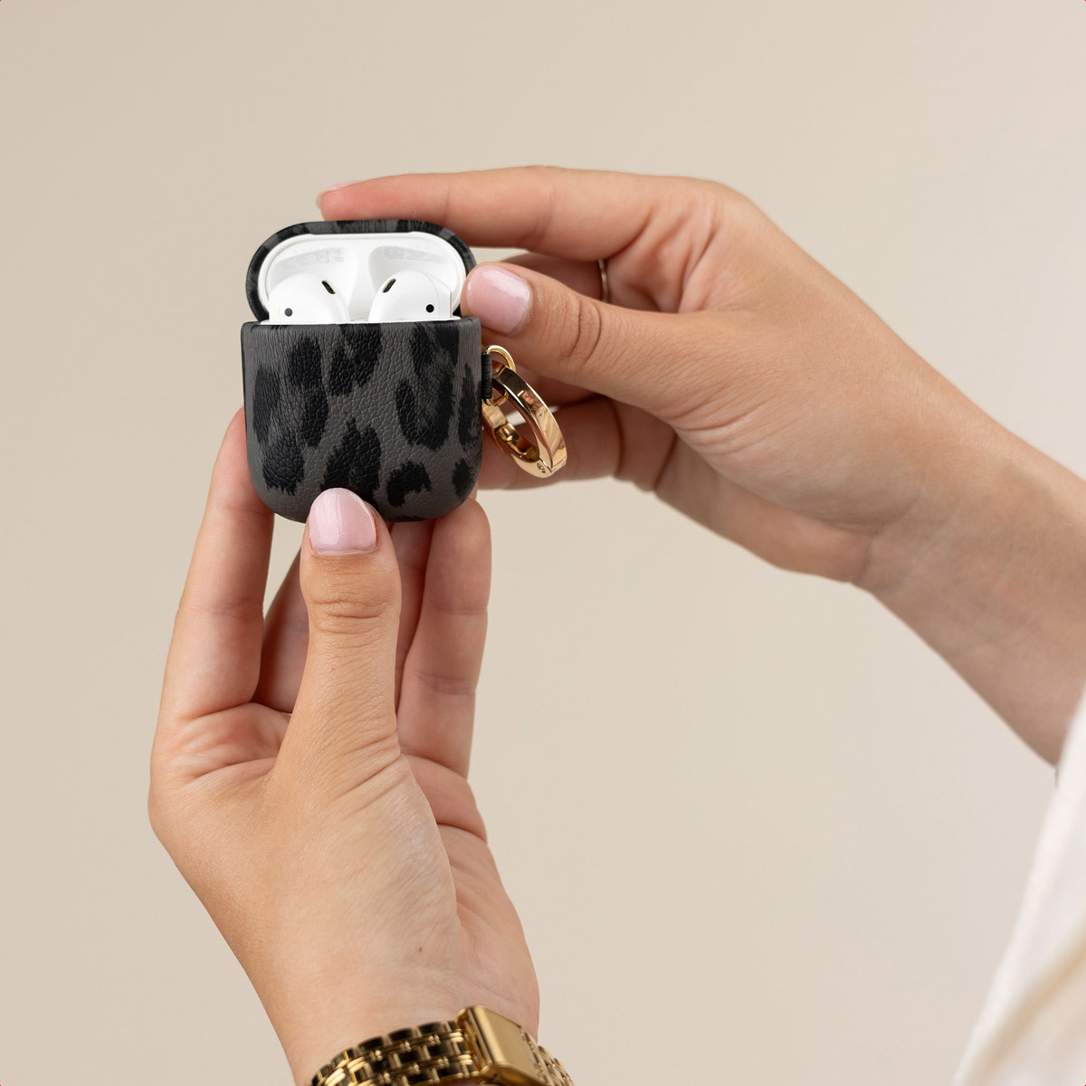 Mani che tengono una custodia per AirPods con motivo grigio e nero e cuffie bianche visibili su sfondo neutro.