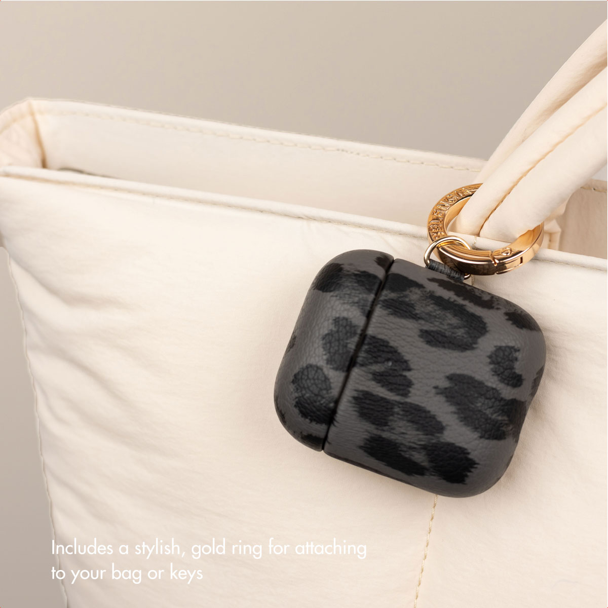 Una custodia per AirPods grigia con motivo leopardato è appesa a un anello d'oro su una borsa bianca.