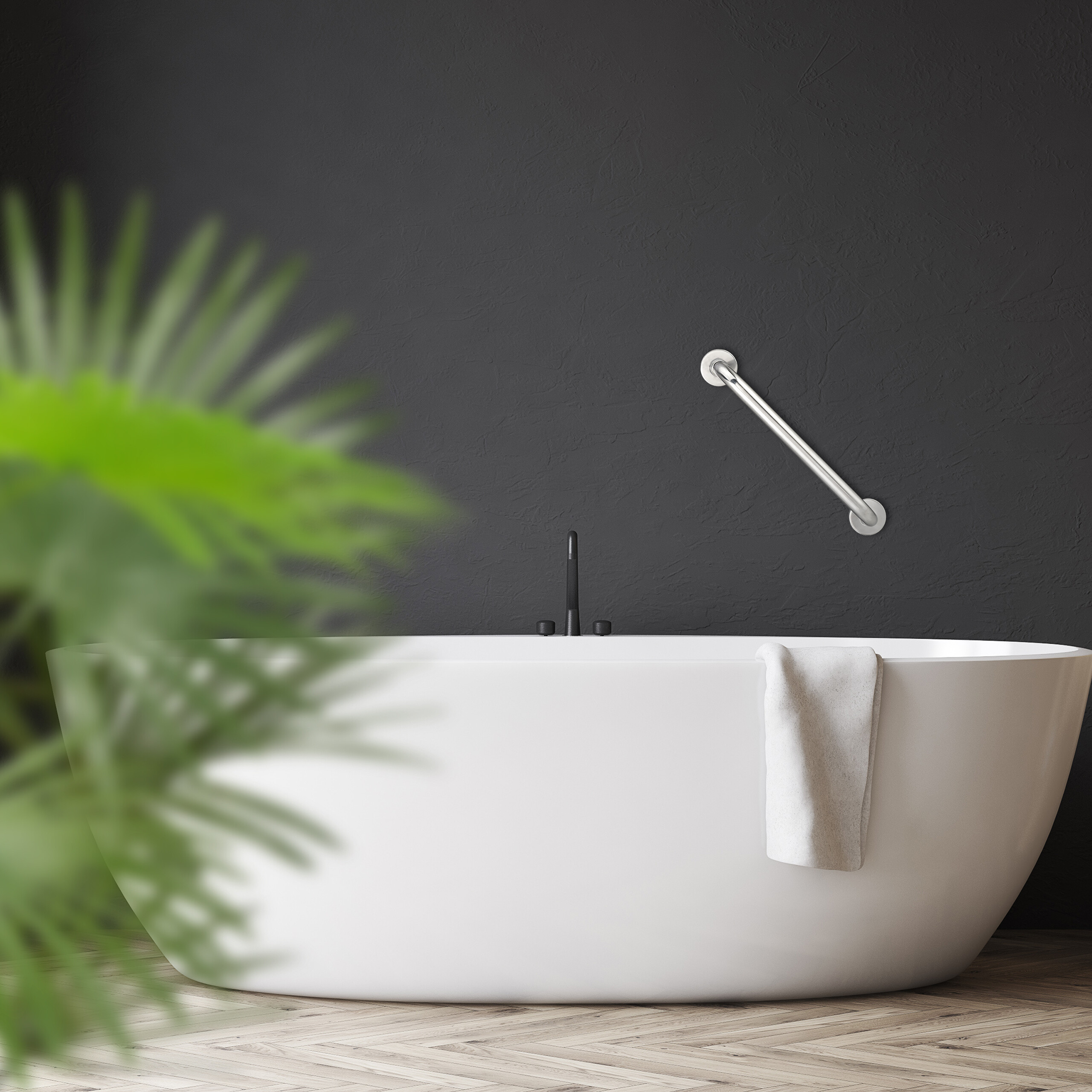 Eine weiße Badewanne vor dunkler Wand, mit Handtuch, Haltegriff und einer unscharfen Pflanze im Vordergrund.