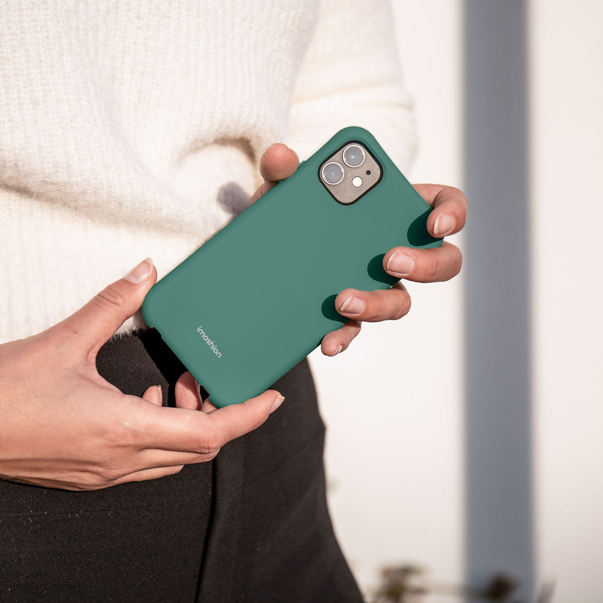 Une personne portant un pull blanc tient une coque de téléphone vert foncé.
