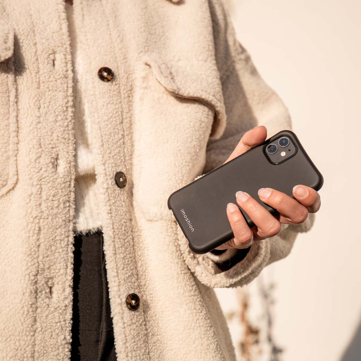 Une personne portant une veste duveteuse crème tient un smartphone noir.