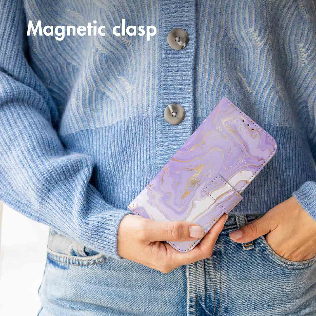 Una persona con suéter de punto azul y vaqueros sostiene una funda con tapa de mármol morado y cierre magnético.