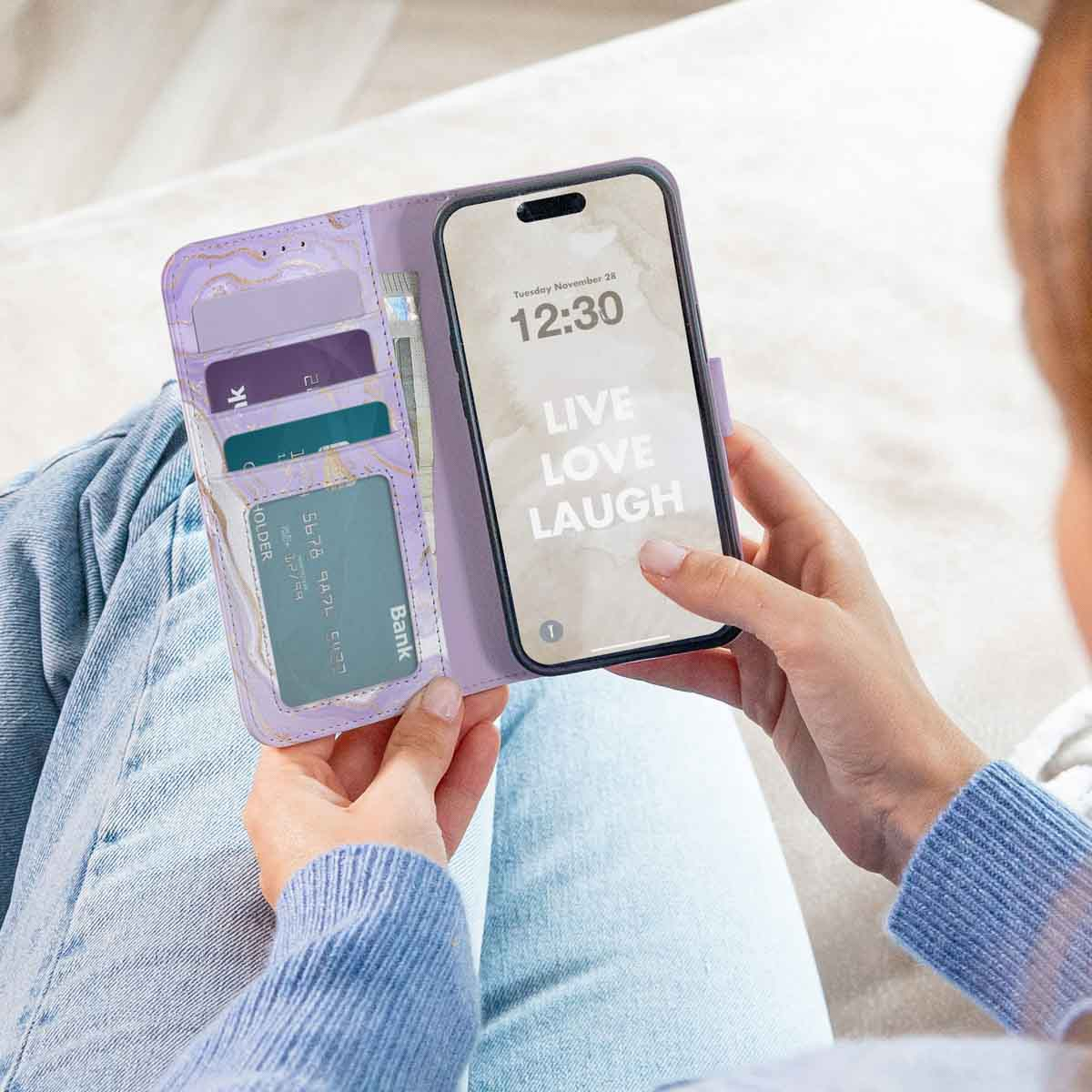 Persona sosteniendo una funda de billetera morada con tarjeteros y un teléfono con Live Love Laugh.
