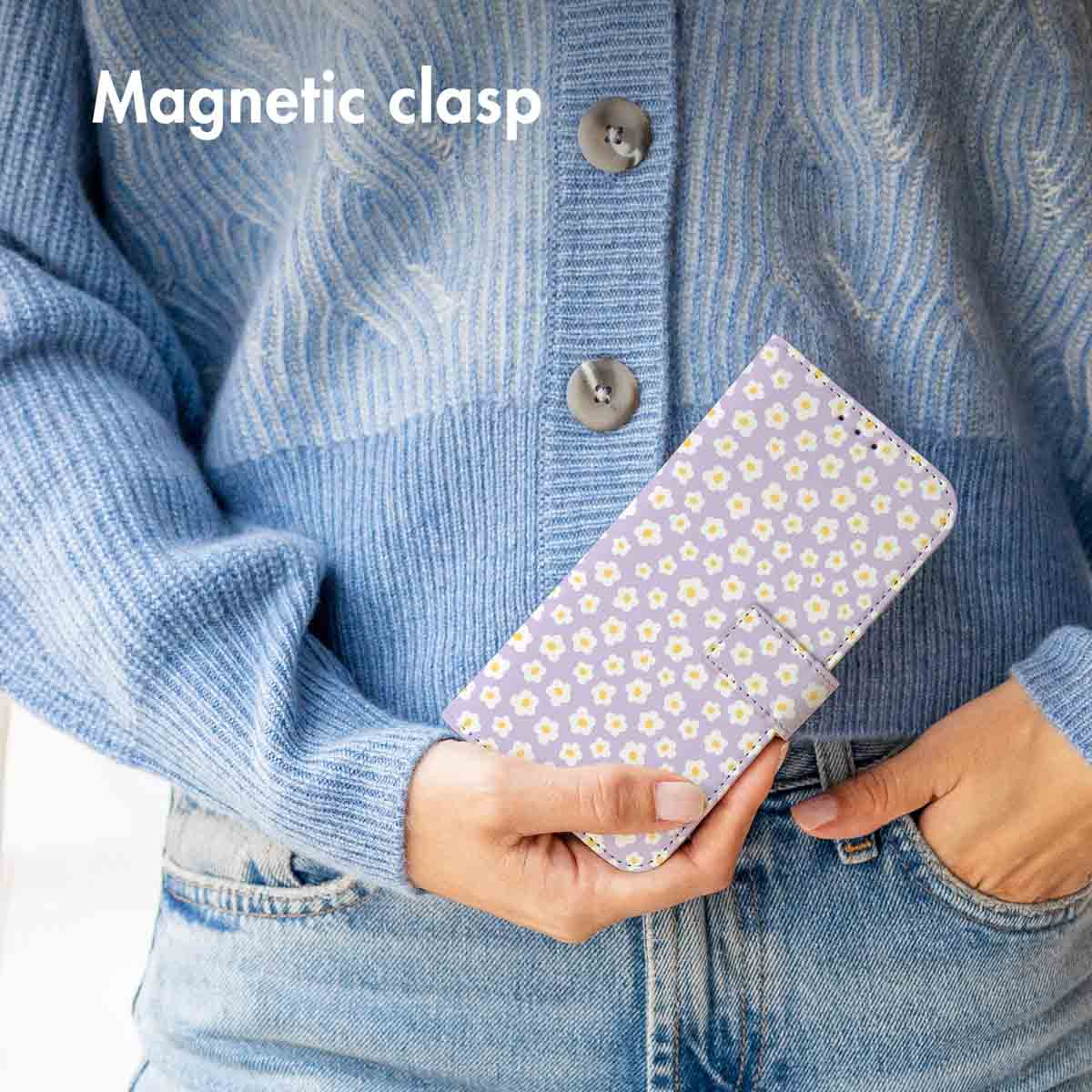 Una persona con suéter de punto azul y jeans sostiene una funda de teléfono morada con flores blancas.